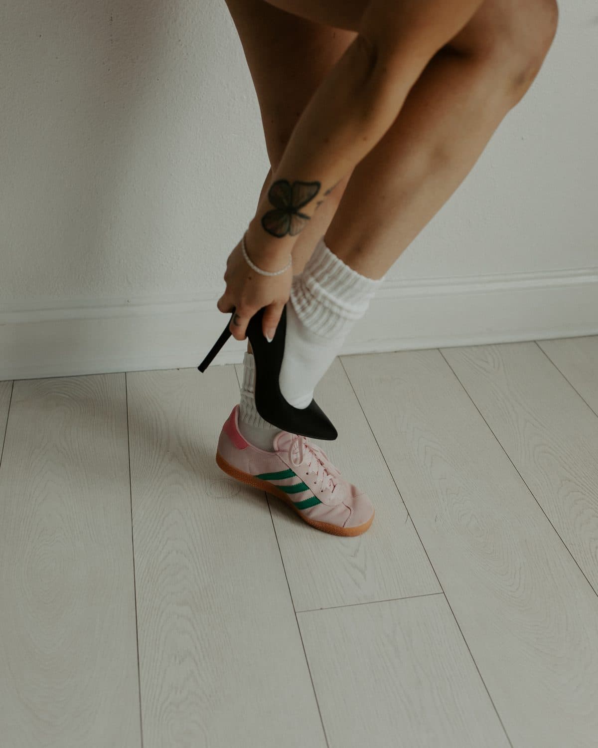 Hand holding a black heel beside a pink sneaker